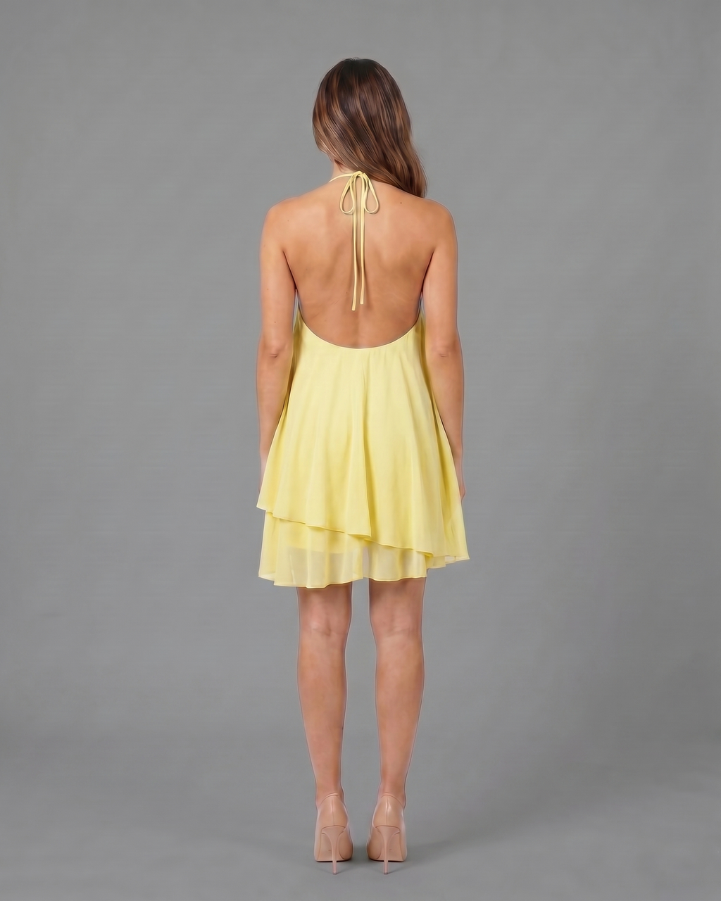 Back view of light yellow halter sleeveless asymmetric mini dress showing open back with halter tie-back