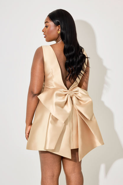 Back detail of women cream mini dress featuring dramatic oversized bow and deep V opening