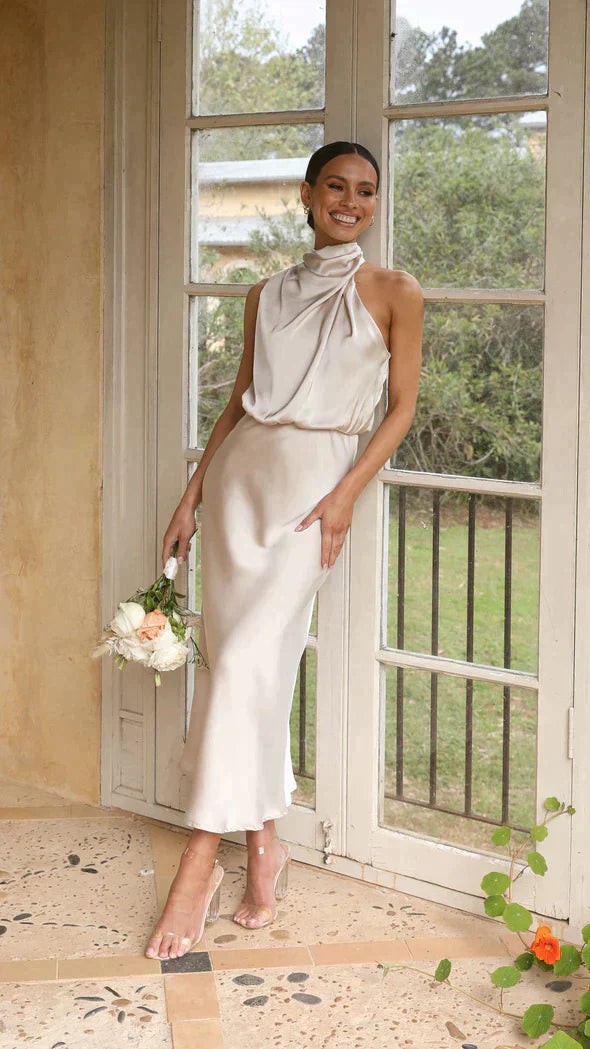 Women cream halter midi dress with draped neckline standing by window