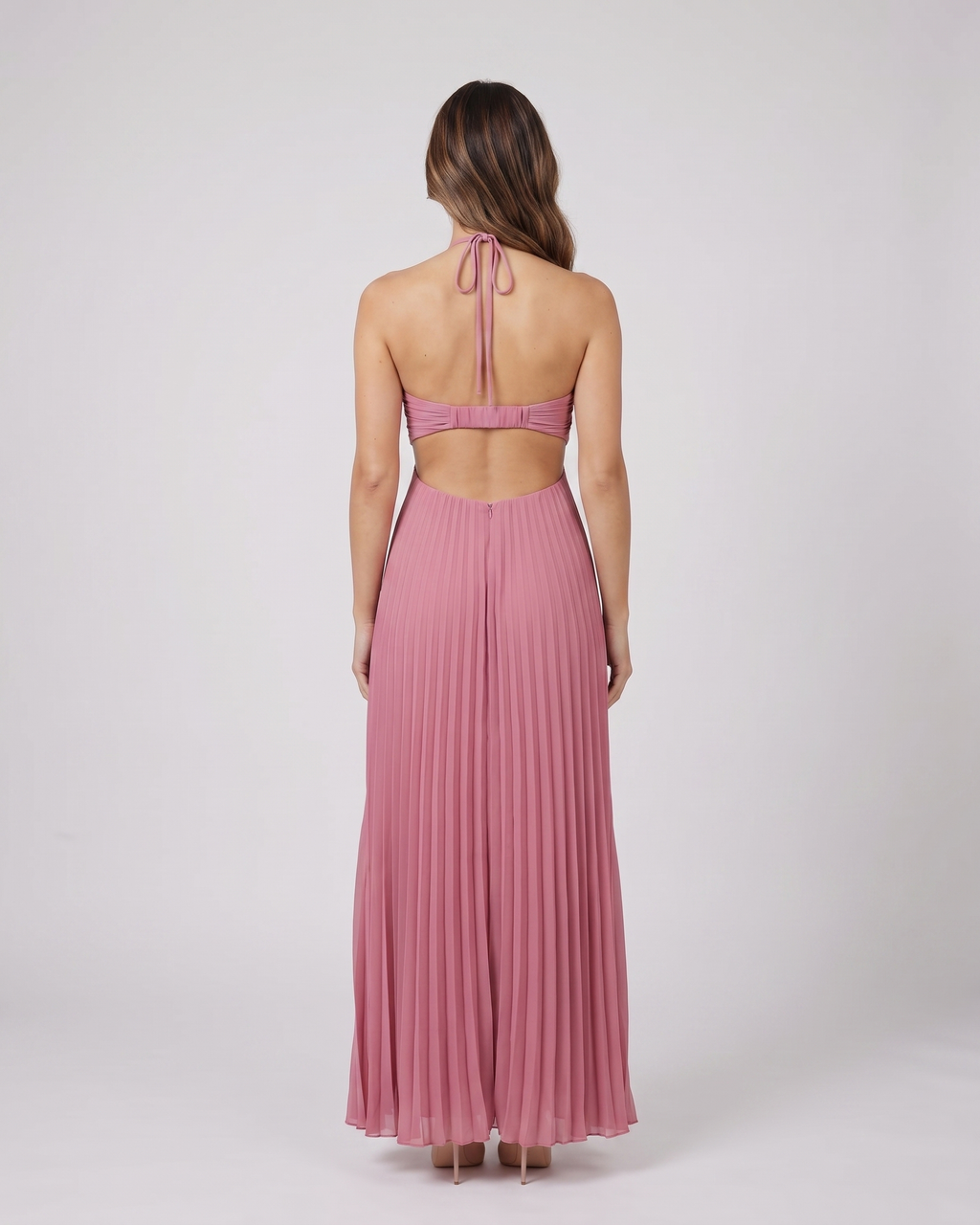 Back view of pink halter pleated with cutout maxi dress showing open back with horizontal mid-back strap and criss-cross tie straps at lower back