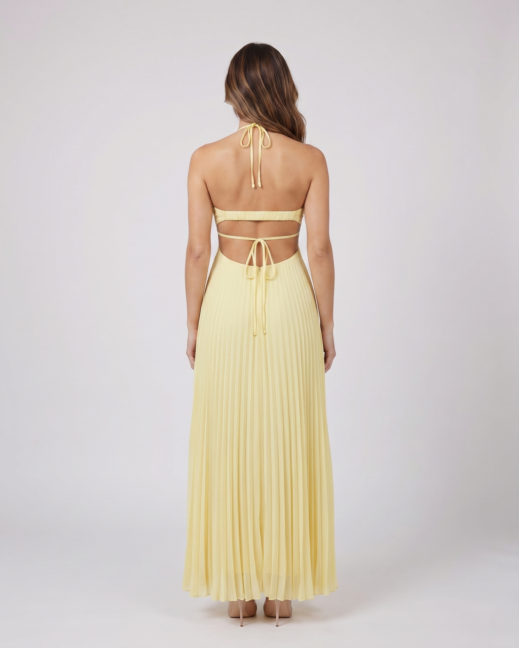 Back view of light canary halter pleated with cutout maxi dress showing open back with horizontal mid-back strap and criss-cross tie straps at lower back