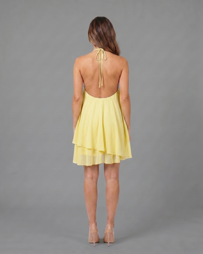Back view of light yellow halter sleeveless asymmetric mini dress showing open back with halter tie-back