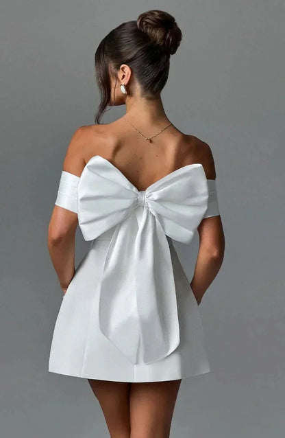 Back view of white mini dress with large bow accent