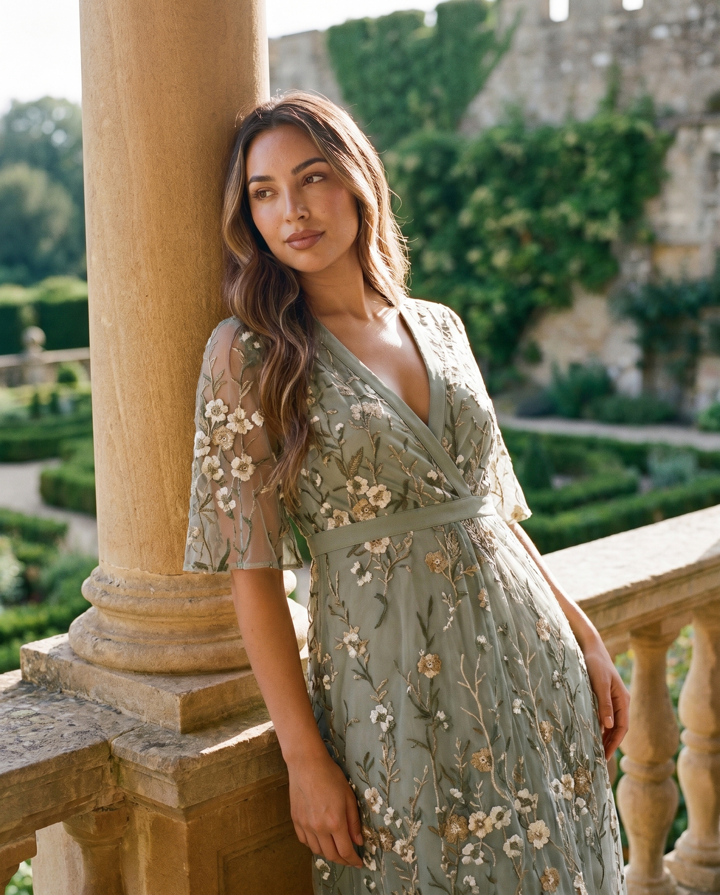 Model wearing sage green embroidered wedding guest maxi dress at grand estate balcony